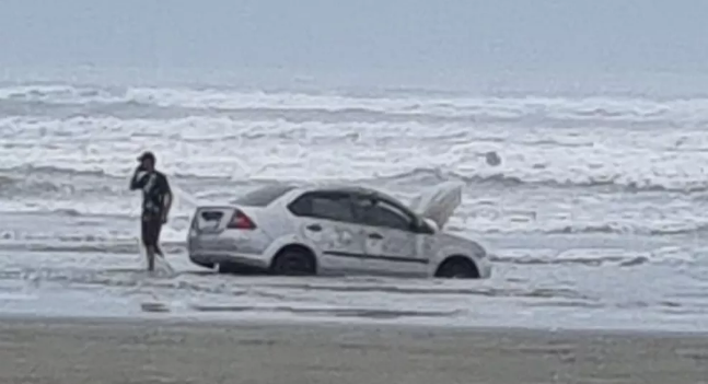Homem usa carro em praia proibida em SP e maré quase leva o veículo